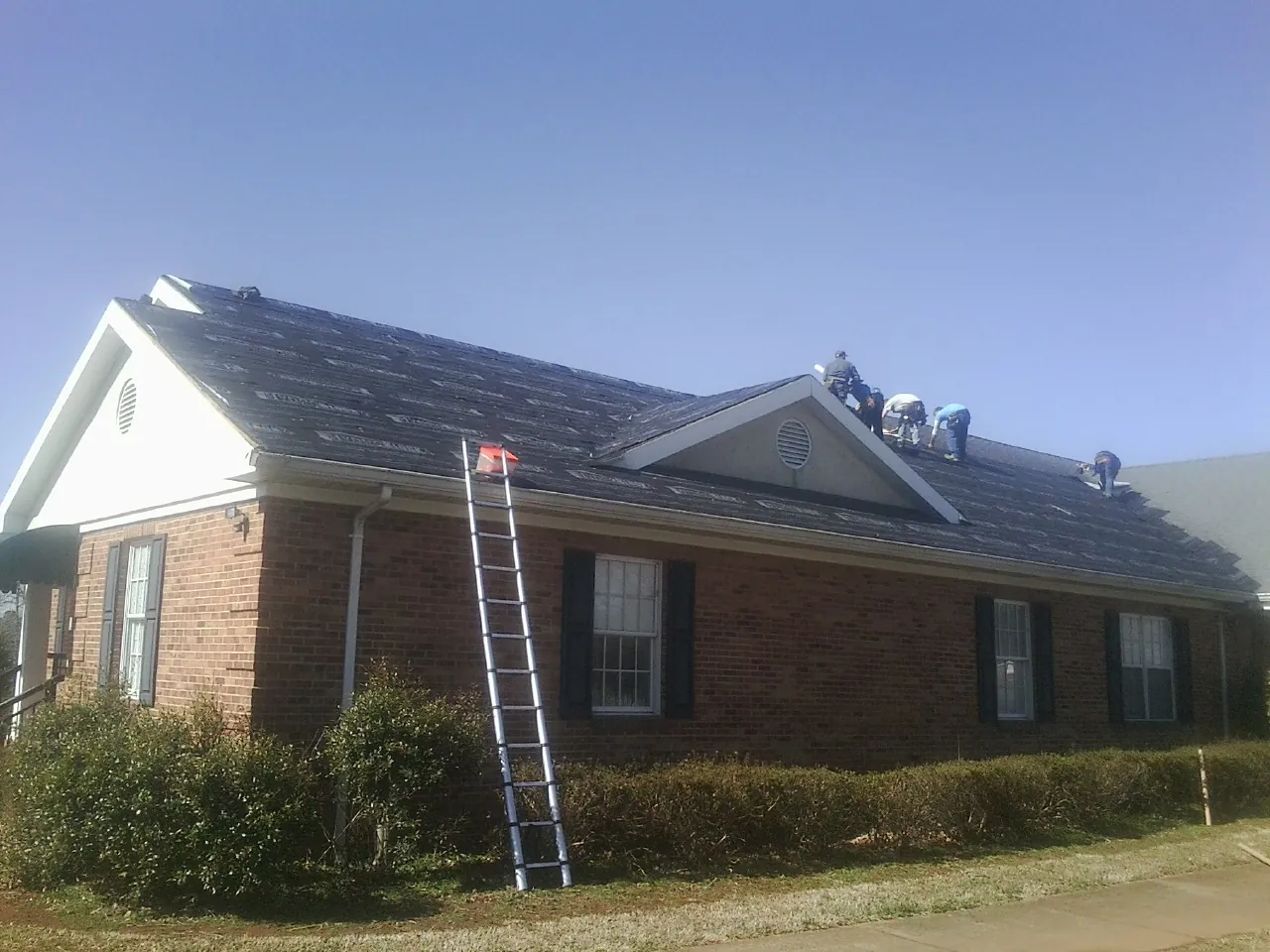 Crew tearing shingles off a brick ranch roof with a ladder set — Emergency Roof Repair work by our crew in Parris Island