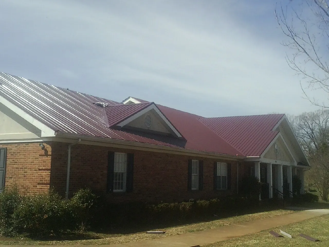 Red metal roof with gabled entries on a long brick building, from a Hail Damage Roof Repair job in Parris Island