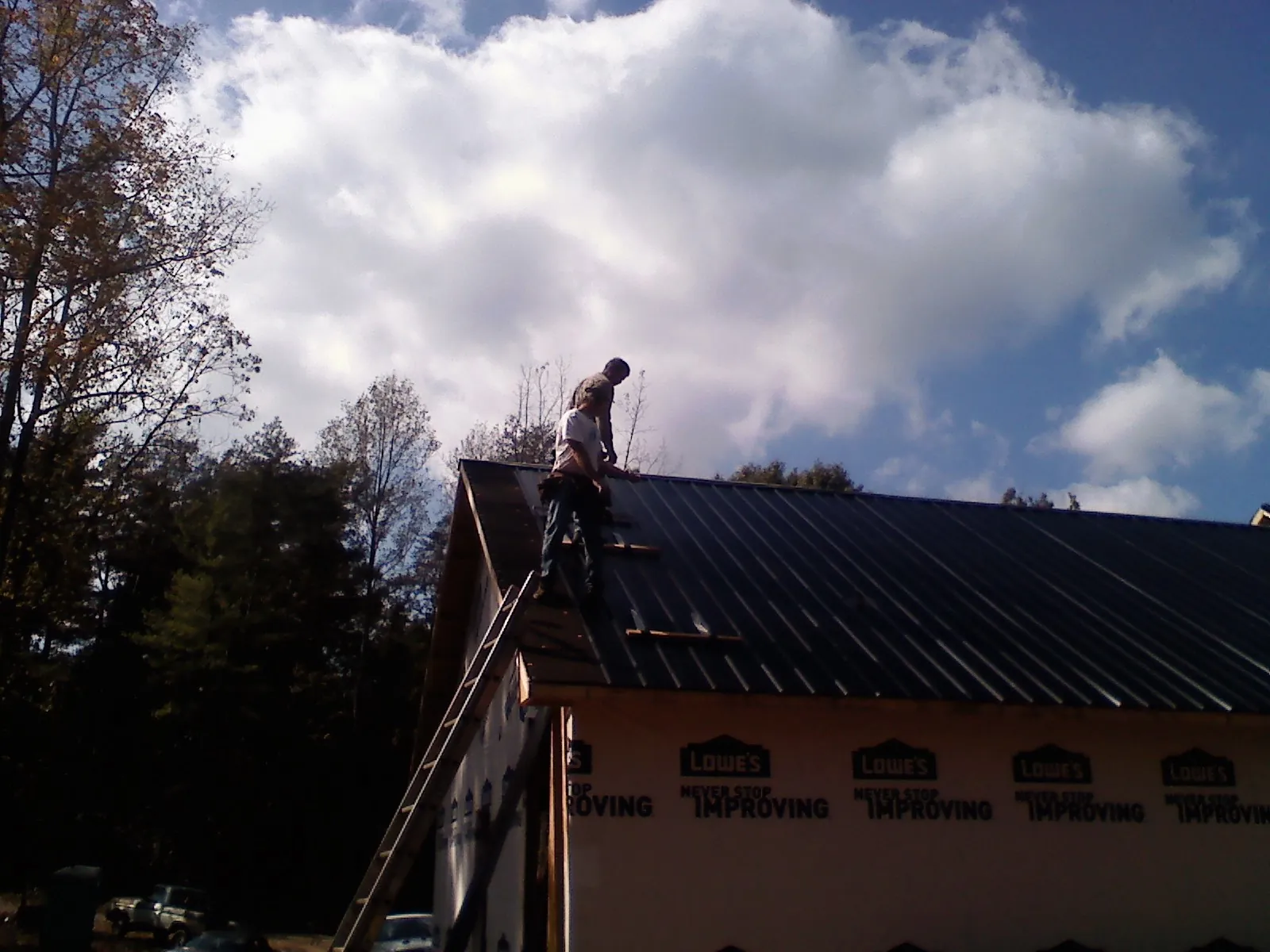 Roofer fastening dark metal panels high against a cloudy sky, from a Roof Inspection job in Parris Island