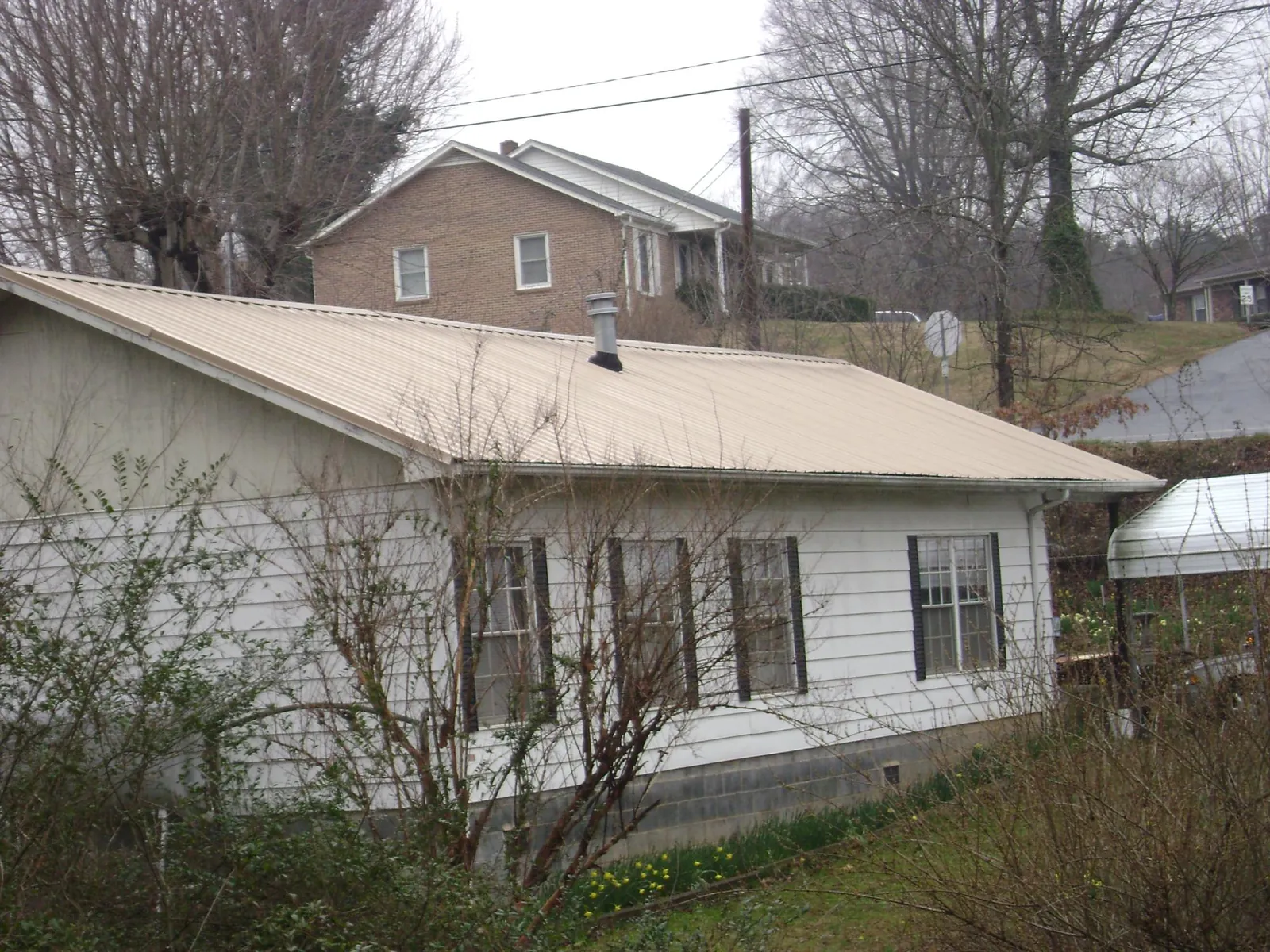 Tan metal roof on a white sided house set into a hillside — Commercial Roofing by Roofing Brothers in Parris Island